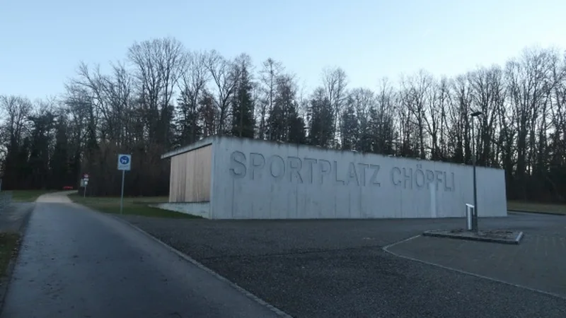 The Sportplatz Chöpfli clubhouse in Hofstetten-Flüh, with its name on the concrete wall and trees behind